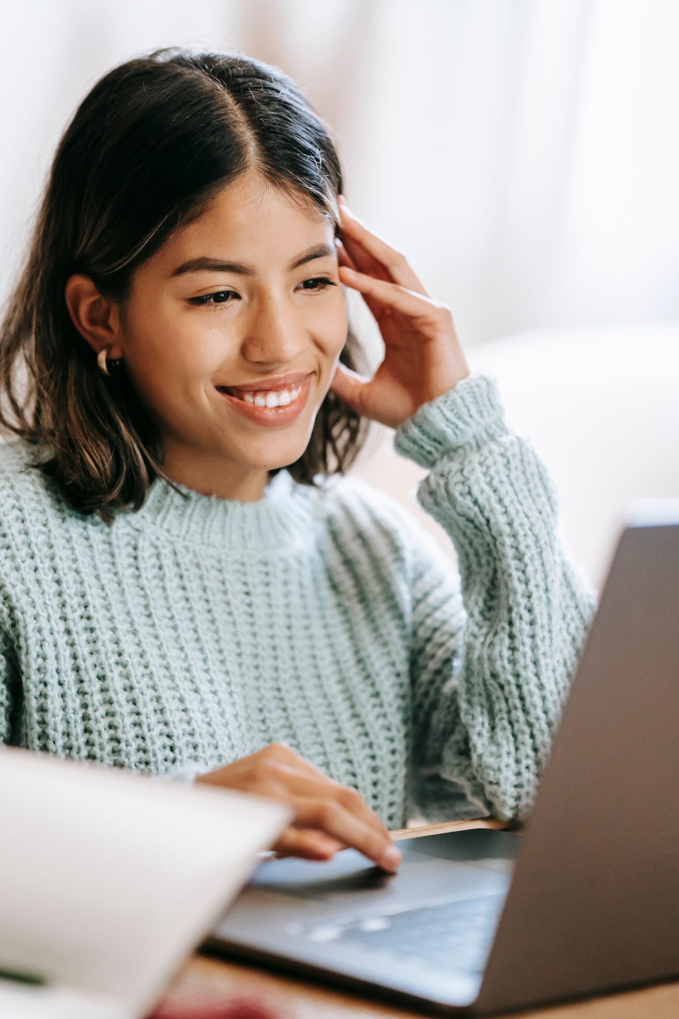 A woman smiling as she works through a course on a laptop at a table at home.
