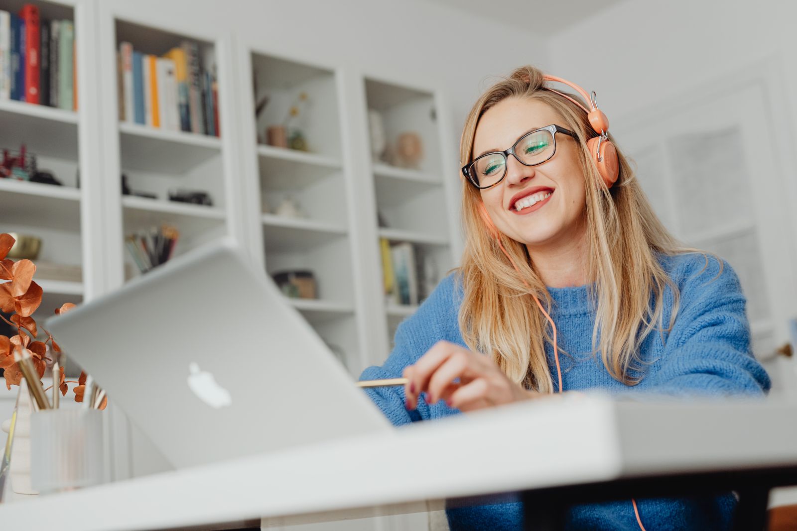 Una mujer sonriendo mientras hace el curso en una computadora port&aacute;til en un escritorio de su casa.